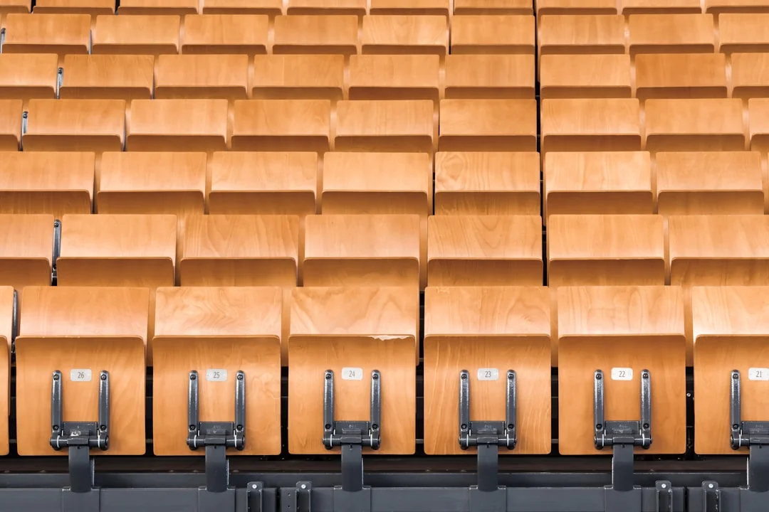 A warmly lit home theater room with two rows of deep-cushioned power recliners facing a large projection screen, beside a sleek ergonomic task chair at a built-in desk nook